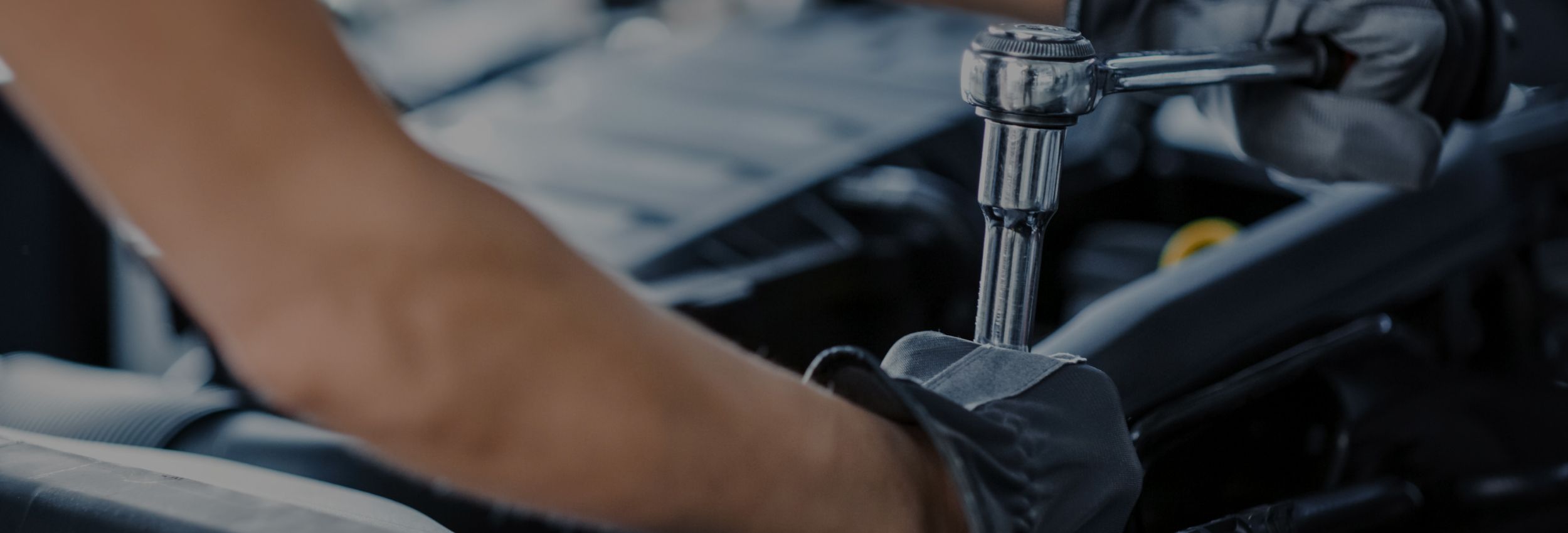 Nahaufnahme eines Mechanikers, der mit einer Ratsche an einem Fahrzeugmotor arbeitet.